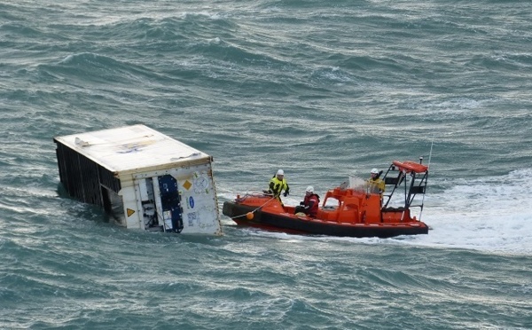 Un conteneur flottant en mer pris en charge par un remorqueur de la Marine